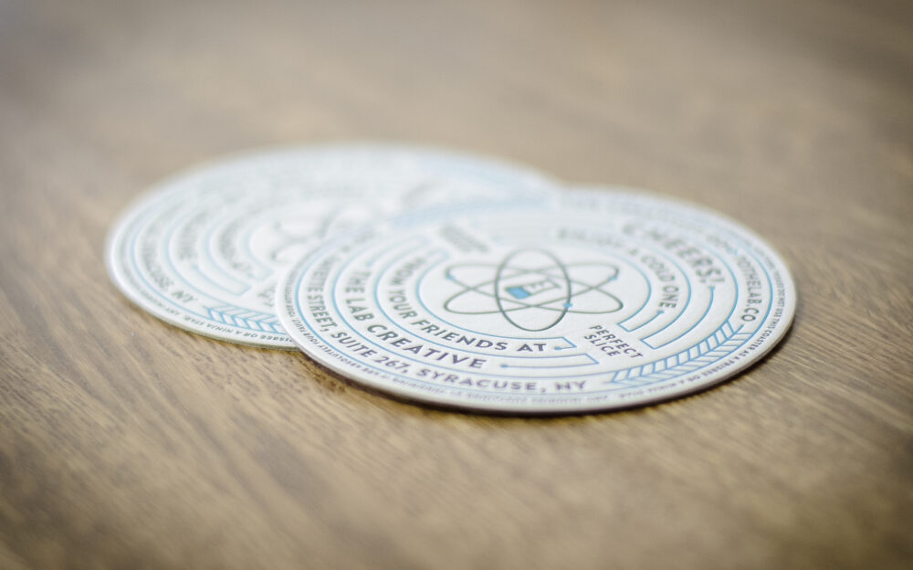 Two letterpress coaster cards with imprints of The Lab Creative brand marks sitting on a wooden table