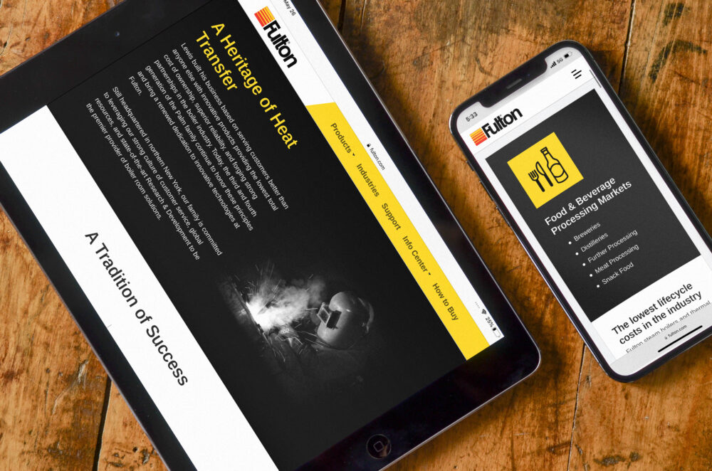 Fulton's responsive About page shown on an iPad and Industry Category page shown on an iPhone 12, both set on a wooden table top