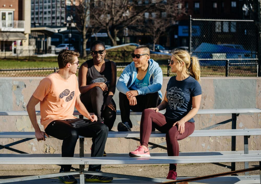 Four diverse young athletes wearing ASICS Runkeeper apparel while having a fun conversation on tiered park benches