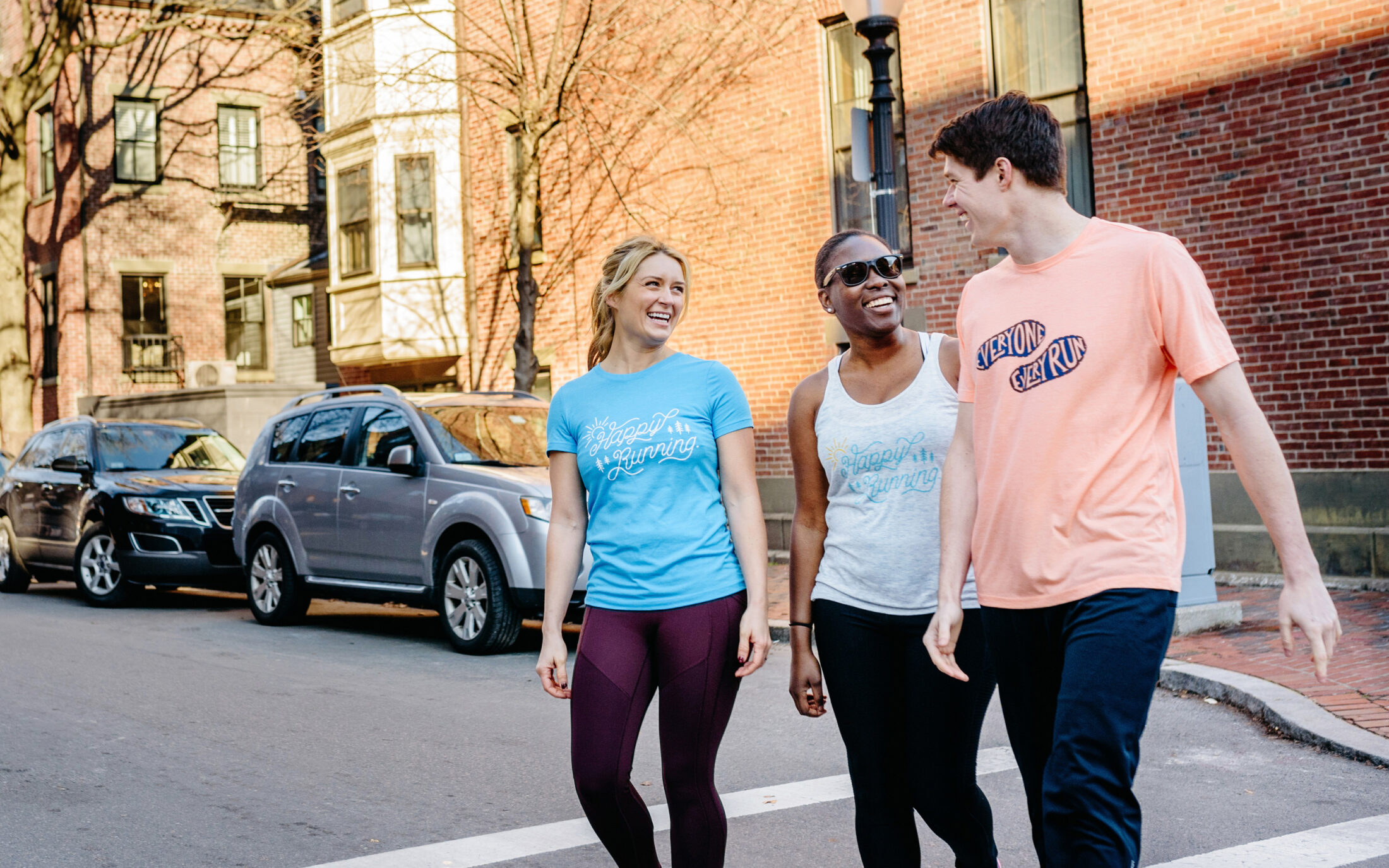 Three young runners walk down a Boston street while wearing ASICS Runkeeper apparel on a sunny morning
