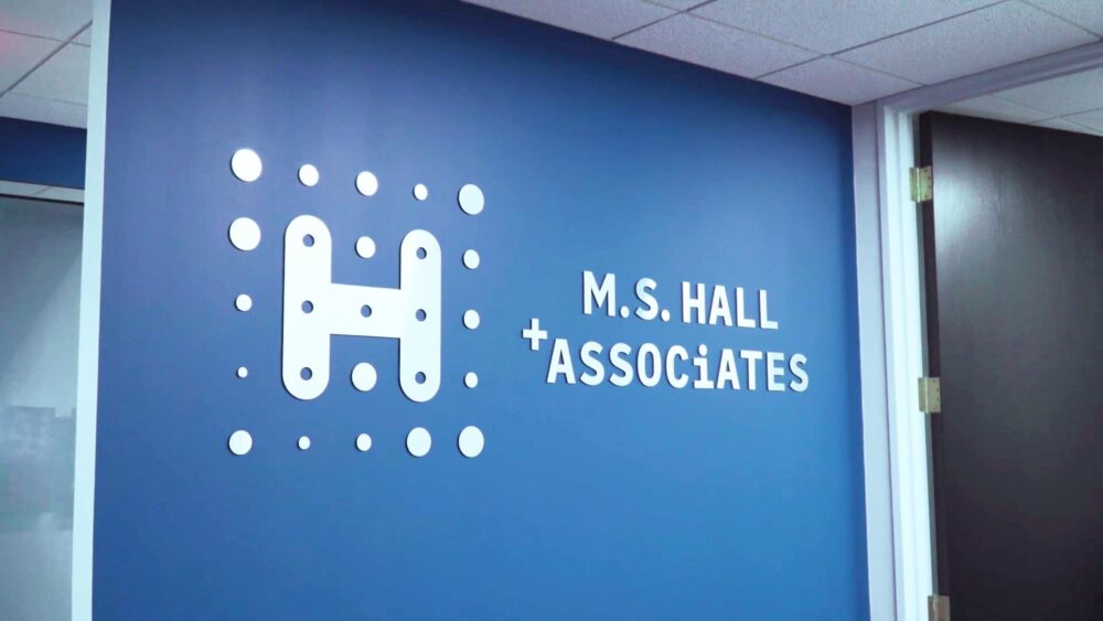 A metal logo for M.S. Hall + Associates installed on the blue wall as seen in the lobby of M.S. Hall + Associates' office