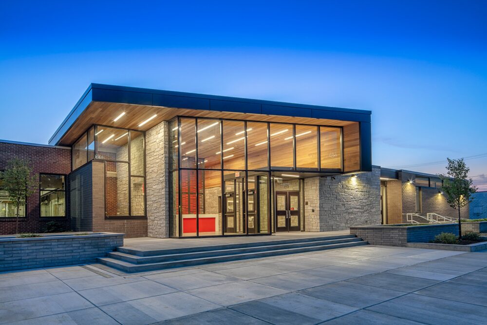 A beautiful contemporary-styled building is lit up from the inside on a Summer evening at the Rescue Mission campus in Syracuse, New York